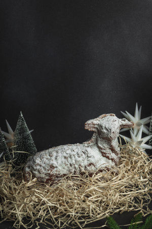 Christmas lamb cake with traditional New Year decor in hay. Baked sweet dessert with sugar icing. Festive background, winter holiday symbol. Dark stone concrete backgroundの写真素材