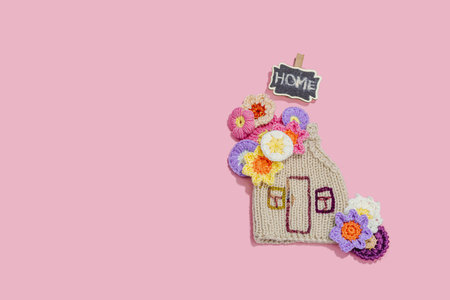 Handmade home spring decor concept. Creative crochet, house figurine, traditional flowers. Festive greeting card, gentle pastel pink background, top viewの写真素材
