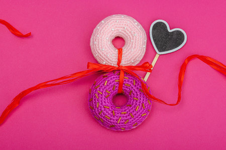 8 made of donuts and red ribbon. Handmade crocheted concept, greeting card, creative craft style. Pink background, flat lay, top viewの写真素材