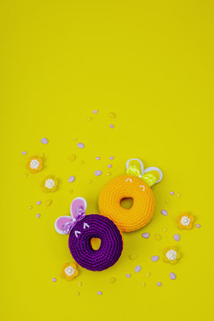 Handmade Easter concept. Crocheted donut bunnies with traditional decoration. Festive symbols, greeting card, flat lay. Creative craft concept, bright yellow background, top viewの写真素材
