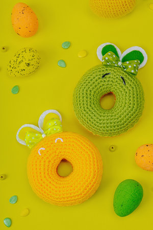 Handmade Easter concept. Crocheted donut bunnies with traditional decoration. Festive symbols, greeting card, flat lay. Creative craft concept, bright yellow background, top viewの写真素材