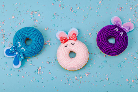 Handmade Easter concept. Crocheted donut bunnies with traditional decoration. Festive symbols, greeting card, flat lay. Creative craft concept, pastel blue background, top viewの写真素材