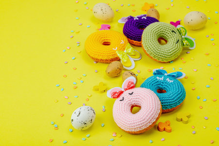 Handmade Easter concept. Crocheted donut bunnies with traditional decoration. Festive symbols, greeting card, flat lay. Creative craft concept, bright yellow background, copy spaceの写真素材