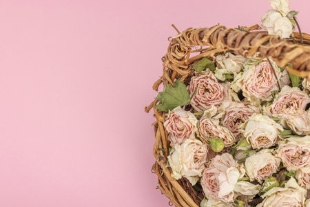 Creative composition with dry delicate roses in homemade wicker basket. Greeting card, pastel pink background, top viewの写真素材