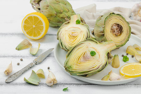 Fresh green artichokes cooking on wooden background. Traditional seasonal ingredients for healthy vegan food, flat lay. Spices, greens, lemon slices, close upの写真素材