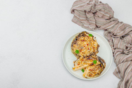 Homemade vegan cabbage steaks with herbs and spices. Healthy food ready to eat on a serving plate, cutlery. Light stone concrete background, top viewの写真素材