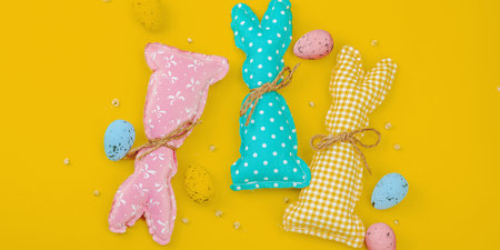 Handmade Easter concept. Sewn textile bunnies with traditional decoration. Festive symbols, greeting card, flat lay. Creative craft concept, bright yellow background, banner formatの写真素材