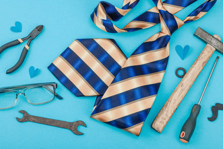 Happy Fathers Day concept. Set of manual tools, tie, spare parts, traditional symbols. Greeting card, flat lay, blue background, top viewの写真素材