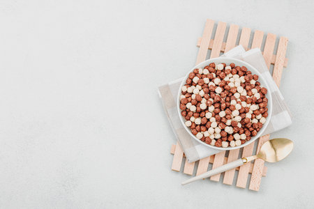 Vegan cereals in balls shape of cocoa and vanilla served with spoon. Full ready bowl to eat, healthy breakfast concept, good morning style. White stone concrete background, top viewの写真素材