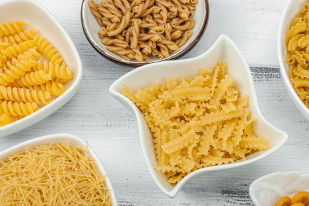 Pasta. Various kinds of uncooked pasta and noodles over wooden background. Traditional Italian ingredient for preparation classic dish. White boards, flat lay, top viewの写真素材