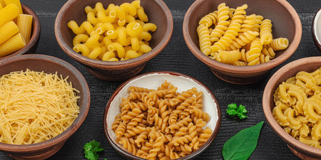 Pasta. Various kinds of uncooked pasta and noodles over wooden background. Traditional Italian ingredient, vegetables and herbs for preparation classic dish. Black boards, flat lay, banner formatの写真素材