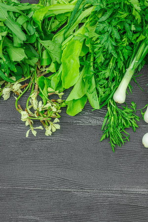 Fresh assorted greens and herbs on a black wooden background. Fragrant dill, onion, parsley, sorrel, lettuce, and arugula. Vegan food, healthy lifestyle, flat lay, top viewの写真素材