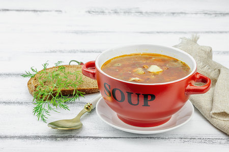 Meat Solyanka soup with sausages, olives and vegetables served on table. Traditional East European dish, bread, cutlery, vintage napkin. Rustic style, wooden boards background, copy spaceの写真素材