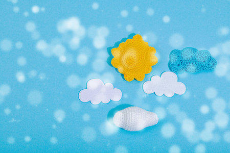 Weather symbols concept. Crocheted sun, clouds and moon. Handmade props, hobby, crafted decor. Hard light, dark shadow, blue background, top viewの写真素材