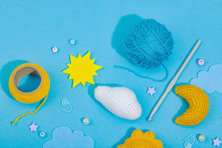 Set of clew of thread for knitting. Crocheted different weather symbols, handmade, creative hobby concept. Props and special craft tools on blue background, top viewの写真素材
