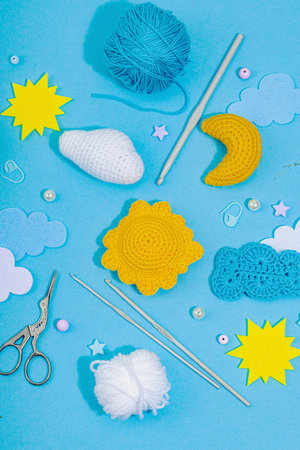 Set of clew of thread for knitting. Crocheted different weather symbols, handmade, creative hobby concept. Props and special craft tools on blue background, top viewの写真素材