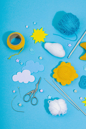 Set of clew of thread for knitting. Crocheted different weather symbols, handmade, creative hobby concept. Props and special craft tools on blue background, top viewの写真素材