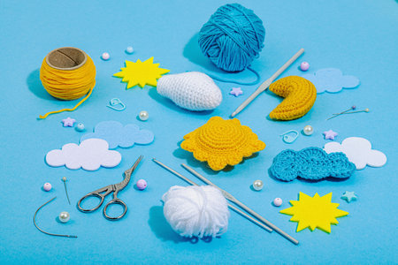 Set of clew of thread for knitting. Crocheted different weather symbols, handmade, creative hobby concept. Props and special craft tools on blue background, close upの写真素材