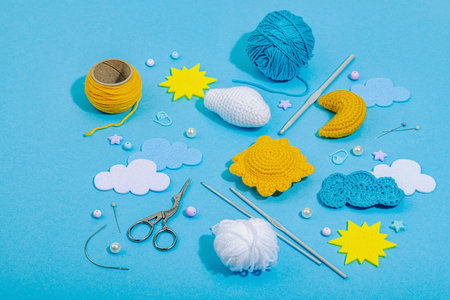 Set of clew of thread for knitting. Crocheted different weather symbols, handmade, creative hobby concept. Props and special craft tools on blue background, close upの写真素材