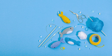 Set of clew of thread for knitting. Crocheted different fishes, handmade, sea hobby concept. Props and special craft tools on blue background, banner formatの写真素材