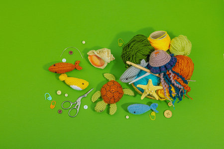 Set of clew of thread for knitting. Crocheted different underwater animals, handmade marine hobby concept. Props and special craft tools on green background, top viewの写真素材