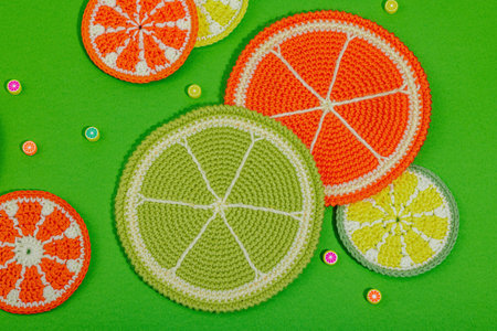 Summer crochet concept. Handmade citrus slices, juicy fruits style. Bright green background, flat lay, hard light, dark shadow, top viewの写真素材