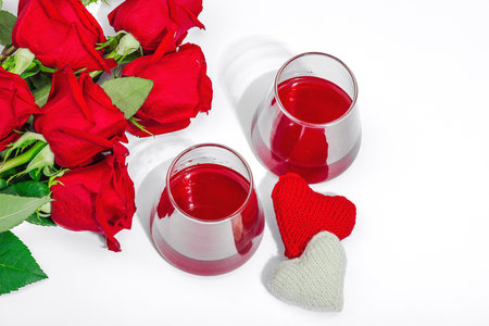 The concept of a romantic date. Two glasses of wine, handmade hearts, a bouquet of red roses. Trendy hard light, dark shadow, white background, flat lay, top viewの写真素材