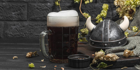 Creative Oktoberfest composition. Dark beer, viking helmet, hop and wheat. German festival food concept. Trendy hard light, dark shadow, vintage black background, banner formatの写真素材