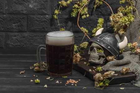 Creative Oktoberfest composition. Dark beer, viking helmet, hop and wheat. German festival food concept. Trendy hard light, dark shadow, vintage black background, copy spaceの写真素材