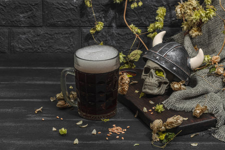 Creative Oktoberfest composition. Dark beer, viking helmet, hop and wheat. German festival food concept. Trendy hard light, dark shadow, vintage black background, copy spaceの写真素材