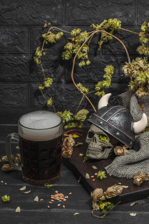 Creative Oktoberfest composition. Dark beer, viking helmet, hop and wheat. German festival food concept. Trendy hard light, dark shadow, vintage black background, close upの写真素材