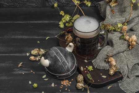 Creative Oktoberfest composition. Dark beer, viking helmet, hop and wheat. German festival food concept. Trendy hard light, dark shadow, vintage black background, copy spaceの写真素材