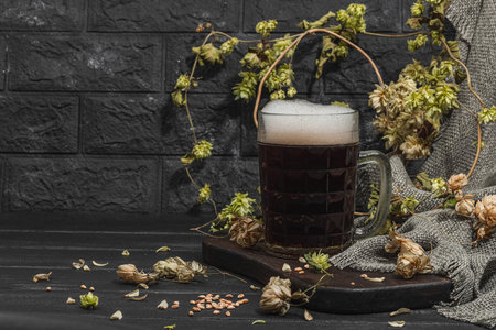 Traditional Oktoberfest composition. Dark beer, hop and wheat. German festival food concept. Trendy hard light, dark shadow, vintage black background, copy spaceの写真素材