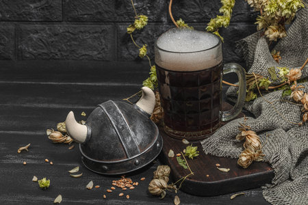 Creative Oktoberfest composition. Dark beer, viking helmet, hop and wheat. German festival food concept. Trendy hard light, dark shadow, vintage black background, copy spaceの写真素材