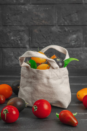 Assortment of various ripe tomatoes in a trendy eco bag. Handmade, zero-waste concept. Black wooden background, copy spaceの写真素材