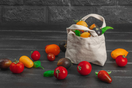 Assortment of various ripe tomatoes in a trendy eco bag. Handmade, zero-waste concept. Black wooden background, copy spaceの写真素材