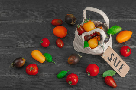 Assortment of various ripe tomatoes in a trendy eco bag. Handmade, Sale zero-waste concept. Black wooden background, top viewの写真素材