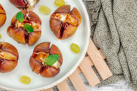 Oven-baked figs with camembert or brie cheese, herbs and honey. Healthy food, seasonal fruits, delicious snack. White wooden background, top viewの写真素材