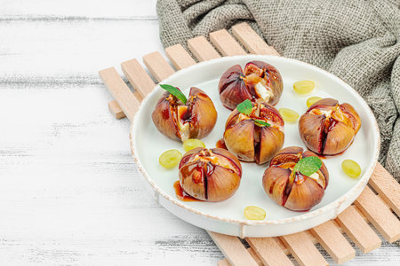 Oven-baked figs with camembert or brie cheese, herbs and honey. Healthy food, seasonal fruits, delicious snack. White wooden background, copy spaceの写真素材