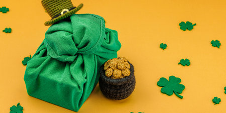 Handmade St. Patrick's Day gift concept. Furoshiki, traditional decorative symbols, crocheted leprechaun hat, pot with golden coins, flat lay, banner formatの写真素材