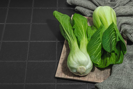 Fresh Bok choy on a trendy black tile background. Traditional Chinese cabbage is a vitamin ingredient used in cooking healthy food. Vegan lifestyle, hard light, dark shadow, flat lay, copy spaceの写真素材