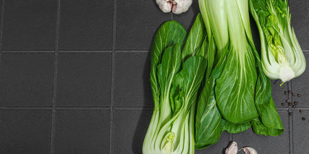 Fresh Bok choy on a trendy black tile background. Traditional Chinese cabbage is a vitamin ingredient used in cooking healthy food. Vegan lifestyle, hard light, dark shadow, flat lay, banner formatの写真素材