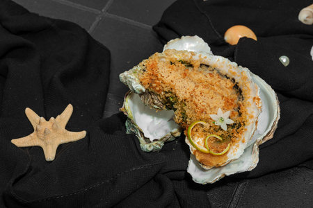 Gourmet baked oyster with herbs and cheese. Elegant seafood dish, coastal culinary delight, healthy ocean-inspired cuisine. Black tile background, marine style, close upの写真素材