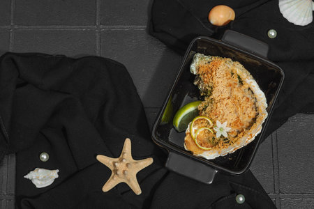 Gourmet baked oyster with herbs and cheese. Elegant seafood dish, coastal culinary delight, healthy ocean-inspired cuisine. Black tile background, marine style, top viewの写真素材