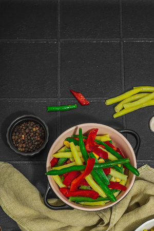 Vibrant vegetable mix with yellow and green beans, red bell peppers. Assorted spices, vegan lifestyle. Black tile background, flat lay, top viewの写真素材