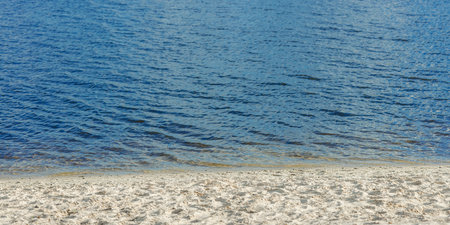 Scenic view of the Dnipro River in Kyiv with soft waves, wet sand, and clear blue water under...