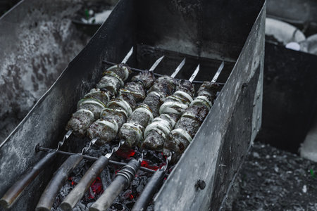 Smoldering charcoal grill with skewered meat at dusk. Outdoor cooking, backyard picnic atmosphere, and street food cultureの写真素材