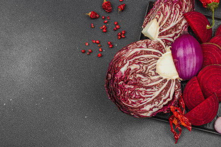 Modern plant-based healthy culinary style. Flat lay of vibrant red beetroot, radicchio, chili peppers, red onions, shallots and pink peppercorns on a dark stone backgroundの写真素材