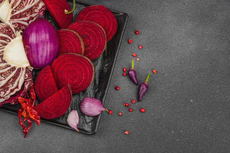 Modern plant-based healthy culinary style. Flat lay of vibrant red beetroot, radicchio, chili peppers, red onions, shallots and pink peppercorns on a dark stone background, top viewの写真素材