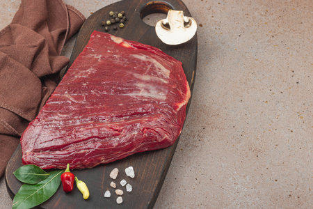 Fresh raw flank steak with assorted spices on wooden cutting board. Culinary concept for meat preparation, gourmet cooking, or food styling, copy spaceの写真素材